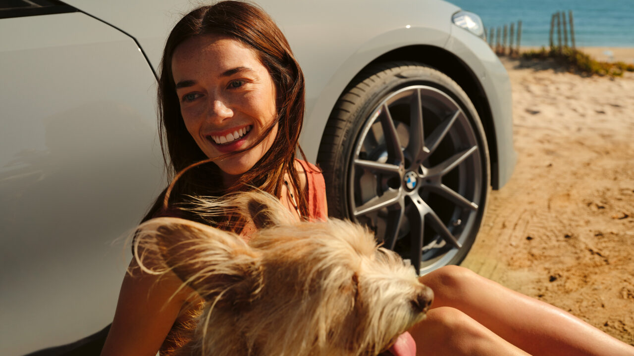 Vrouw zit op het strand met haar hond naast een BMW